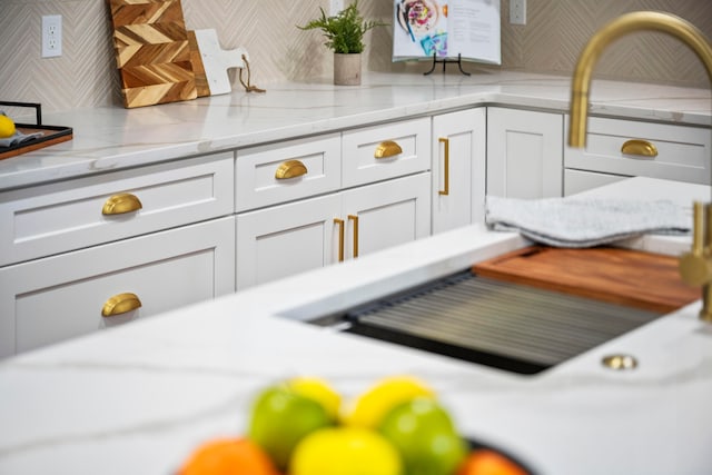 room details featuring decorative backsplash, white cabinets, and light stone counters