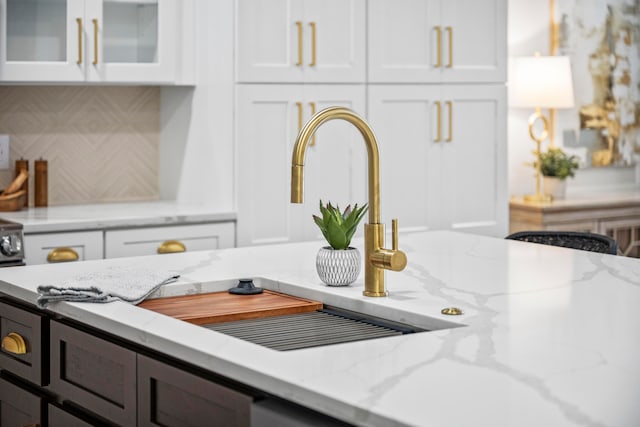 details with white cabinetry, light stone countertops, sink, and backsplash