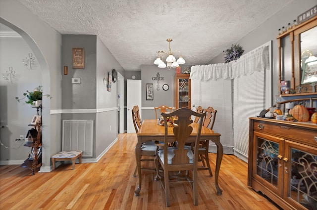 dining area with light hardwood / wood-style flooring, a textured ceiling, and a notable chandelier