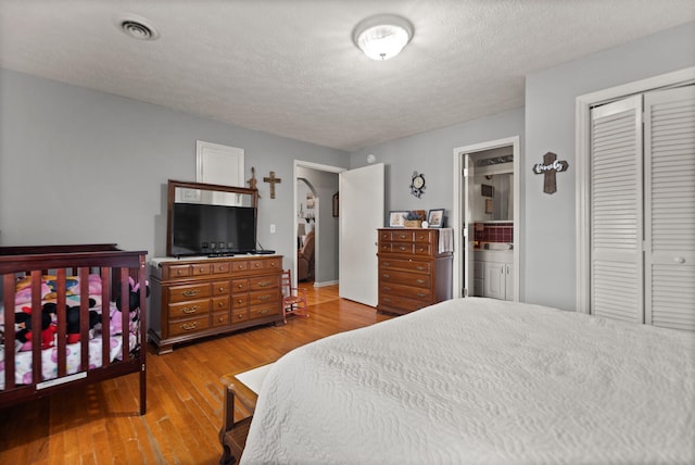 bedroom with a closet, a textured ceiling, ensuite bathroom, and wood-type flooring