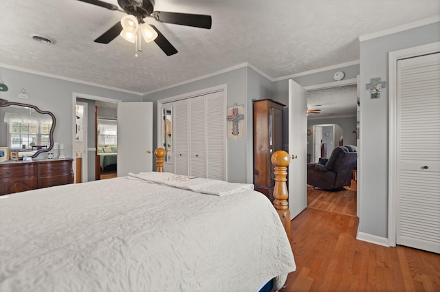 bedroom featuring ceiling fan, crown molding, two closets, and hardwood / wood-style floors