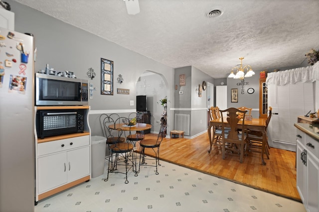 dining area featuring light hardwood / wood-style flooring, a textured ceiling, and a notable chandelier