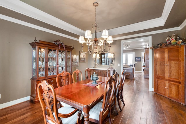 dining area featuring ornamental molding, dark wood-type flooring, a tray ceiling, and an inviting chandelier