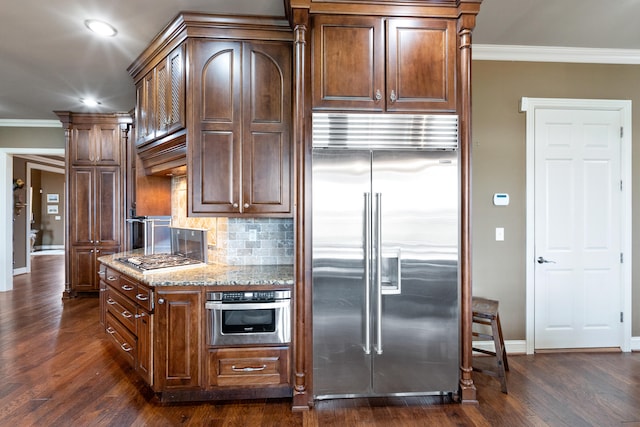 kitchen with dark wood-type flooring, decorative columns, ornamental molding, light stone countertops, and appliances with stainless steel finishes