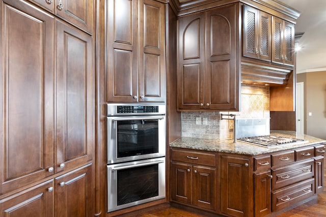 kitchen with light stone counters, appliances with stainless steel finishes, tasteful backsplash, dark hardwood / wood-style floors, and crown molding