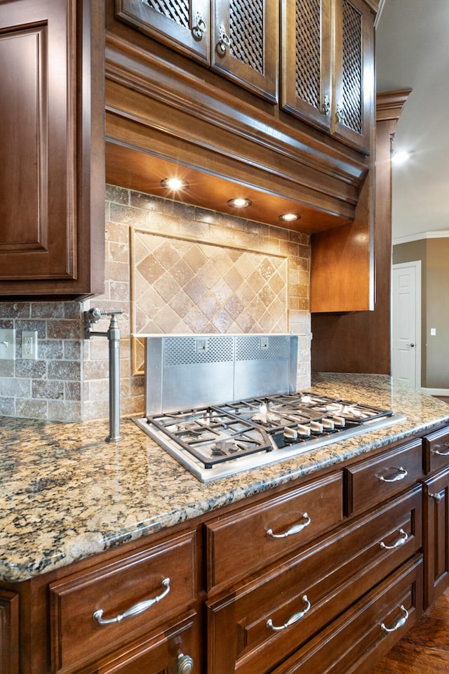 kitchen featuring ornamental molding, tasteful backsplash, light stone countertops, dark hardwood / wood-style floors, and stainless steel gas stovetop