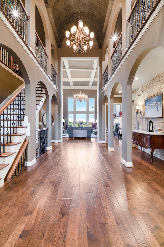 entrance foyer with a high ceiling, an inviting chandelier, coffered ceiling, and hardwood / wood-style floors