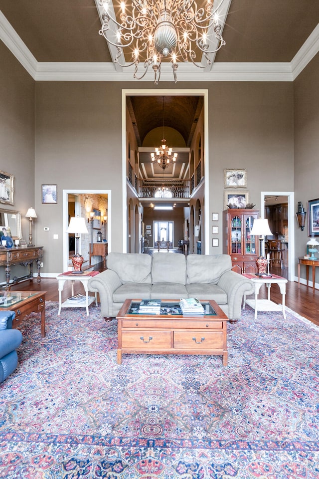 living room with a high ceiling, wood-type flooring, a chandelier, and crown molding