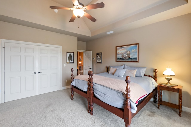 bedroom featuring a closet, light colored carpet, a tray ceiling, lofted ceiling, and ceiling fan