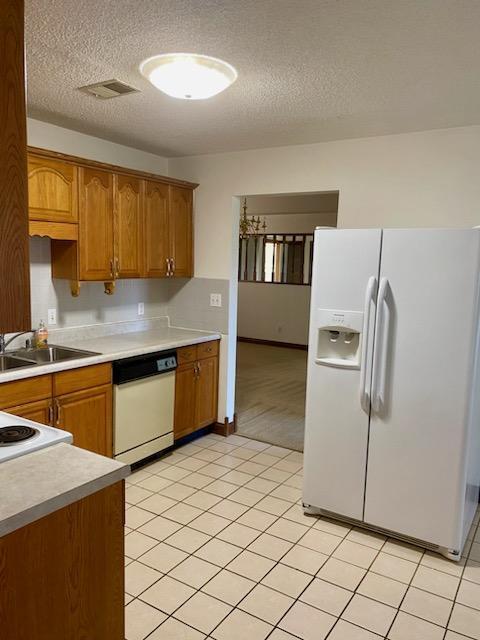 kitchen featuring sink, white appliances, a textured ceiling, and light tile patterned floors