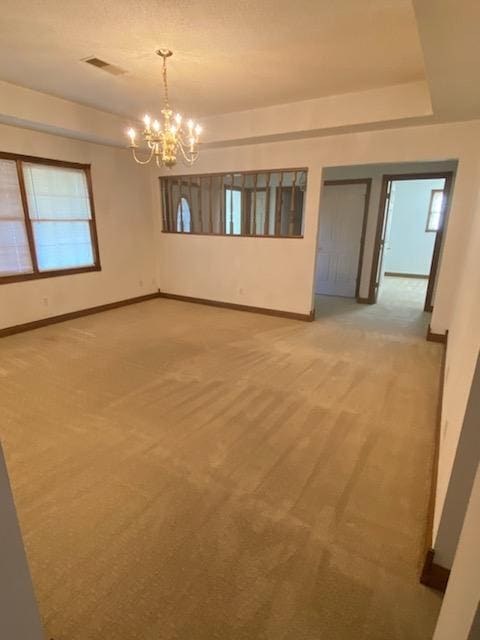 carpeted empty room featuring an inviting chandelier and a raised ceiling