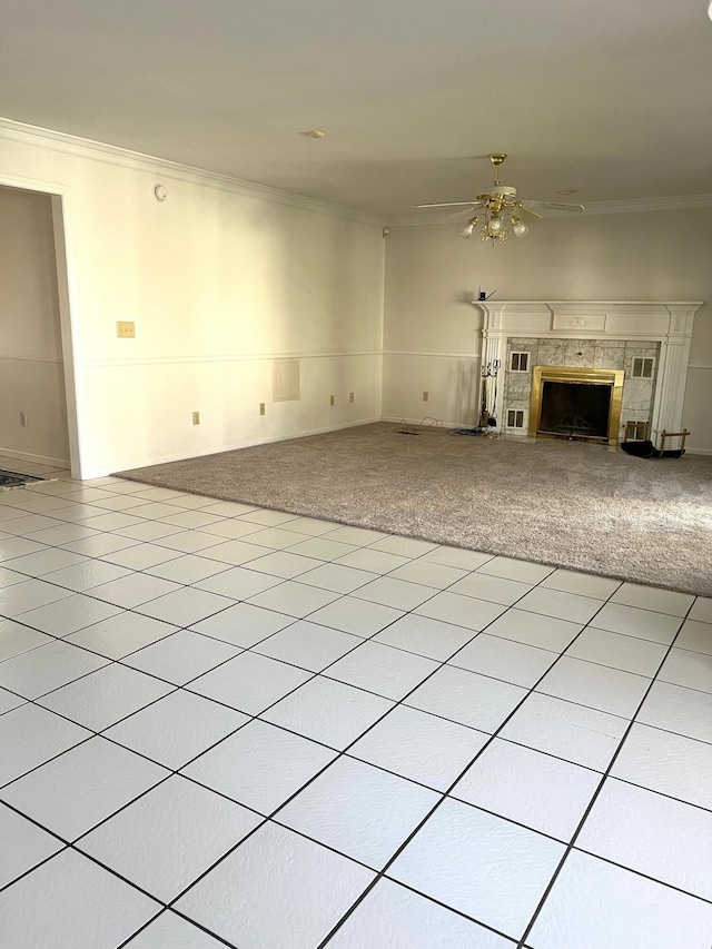 unfurnished living room with a ceiling fan, light colored carpet, a tile fireplace, ornamental molding, and light tile patterned flooring