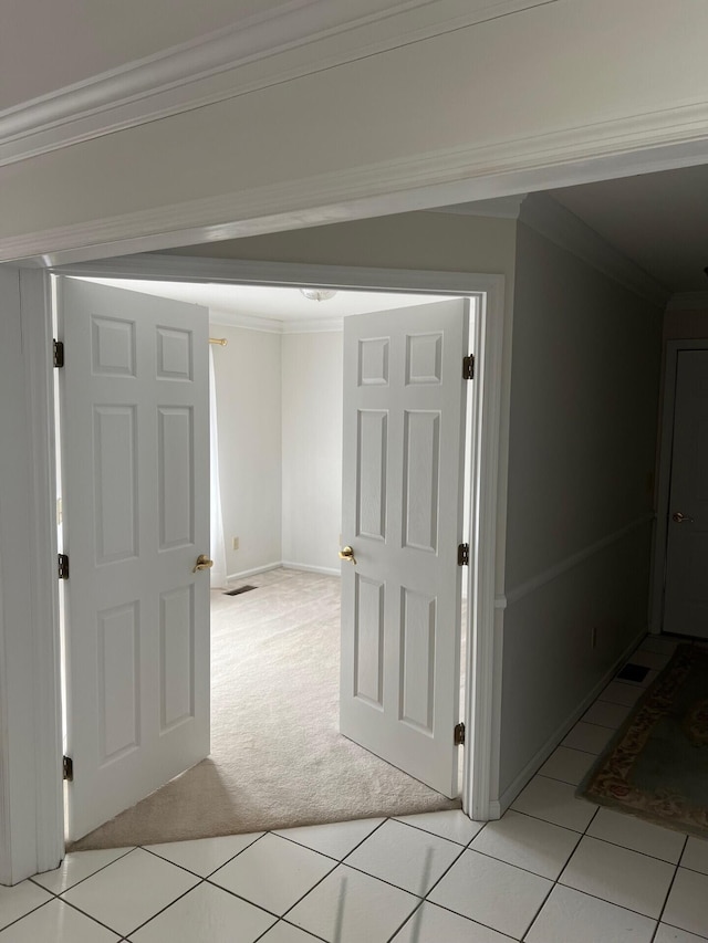 hallway with light carpet, crown molding, baseboards, and light tile patterned floors