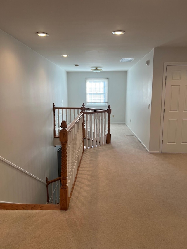 corridor with baseboards, light carpet, visible vents, and an upstairs landing