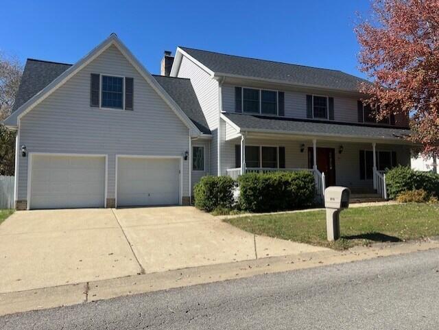 traditional home with a porch, concrete driveway, a chimney, and a front lawn