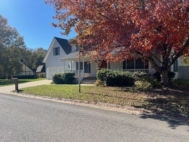 view of property hidden behind natural elements featuring a porch, a garage, a front lawn, and concrete driveway