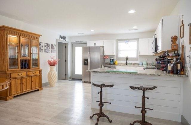 kitchen with white cabinetry, light stone countertops, appliances with stainless steel finishes, and kitchen peninsula