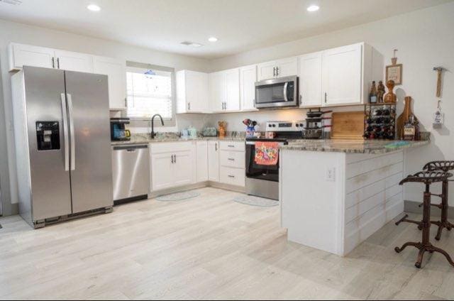 kitchen featuring kitchen peninsula, white cabinetry, light hardwood / wood-style flooring, stone countertops, and stainless steel appliances