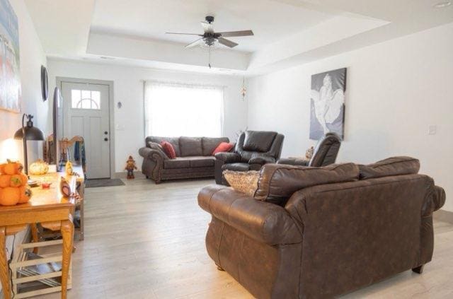 living room featuring light wood-type flooring, a tray ceiling, a wealth of natural light, and ceiling fan