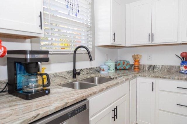 kitchen with light stone countertops, sink, white cabinetry, and dishwasher