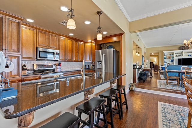 kitchen featuring dark hardwood / wood-style flooring, crown molding, decorative light fixtures, a breakfast bar, and appliances with stainless steel finishes