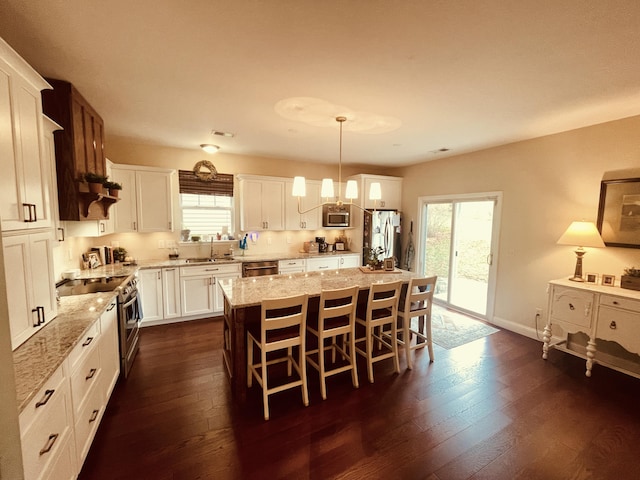 kitchen with a center island, appliances with stainless steel finishes, white cabinetry, hanging light fixtures, and a kitchen breakfast bar