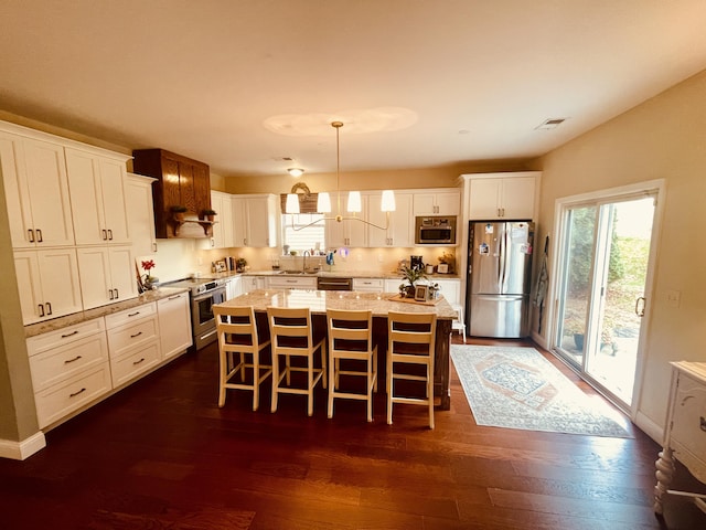 kitchen featuring white cabinets, appliances with stainless steel finishes, a center island, hanging light fixtures, and a breakfast bar