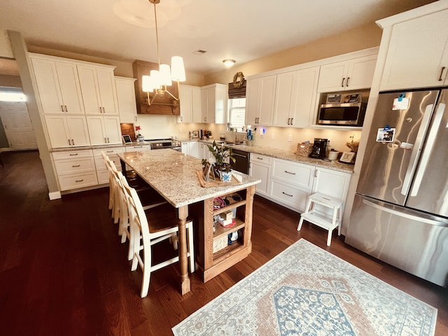 kitchen with light stone countertops, appliances with stainless steel finishes, white cabinets, a kitchen island, and pendant lighting