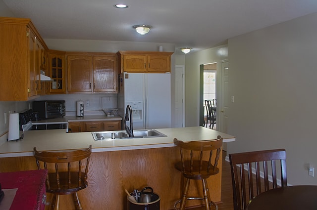 kitchen with a breakfast bar area, sink, white fridge with ice dispenser, and kitchen peninsula