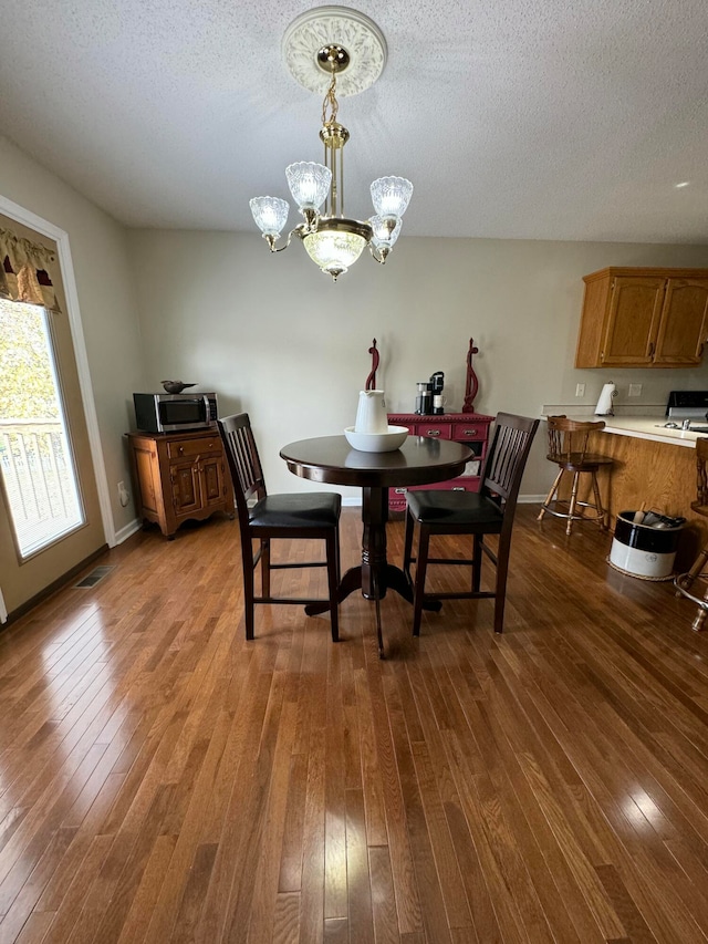 dining area with a textured ceiling, dark wood-type flooring, and a chandelier