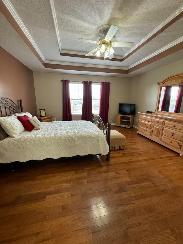 bedroom featuring wood-type flooring, a textured ceiling, ceiling fan, crown molding, and a tray ceiling