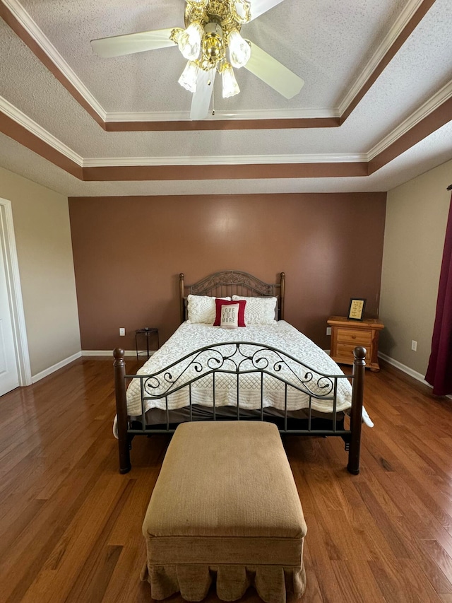 bedroom featuring ceiling fan, ornamental molding, a raised ceiling, and wood-type flooring