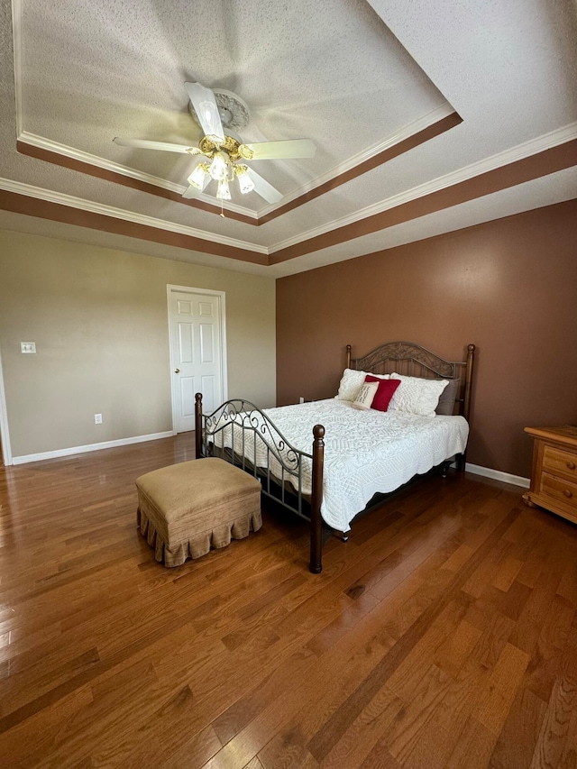 bedroom with wood-type flooring, ceiling fan, and a tray ceiling