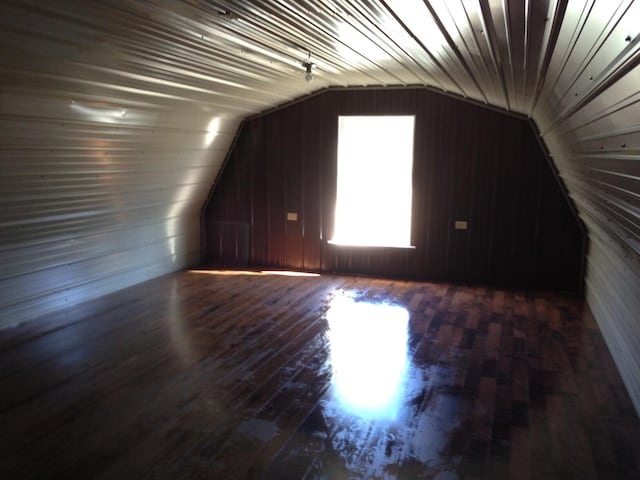 additional living space with dark wood-type flooring, wooden walls, and vaulted ceiling