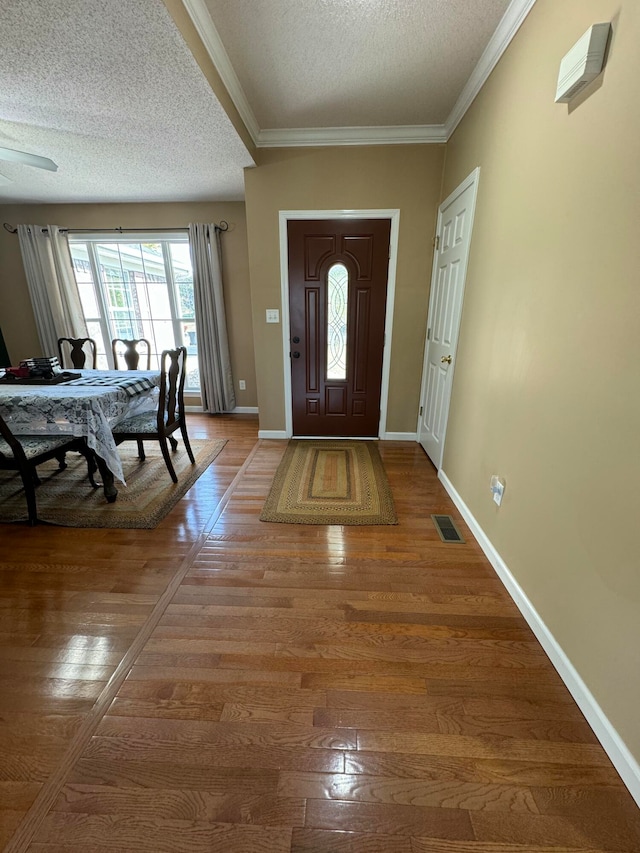 entryway with wood-type flooring, a textured ceiling, crown molding, and ceiling fan