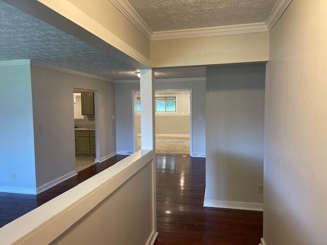 corridor with dark wood-type flooring, a textured ceiling, and ornamental molding