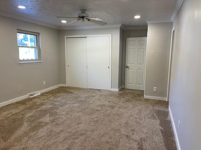 unfurnished bedroom featuring ceiling fan, a textured ceiling, carpet flooring, ornamental molding, and a closet