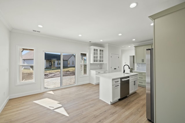 kitchen featuring appliances with stainless steel finishes, sink, decorative backsplash, a kitchen island with sink, and light wood-type flooring