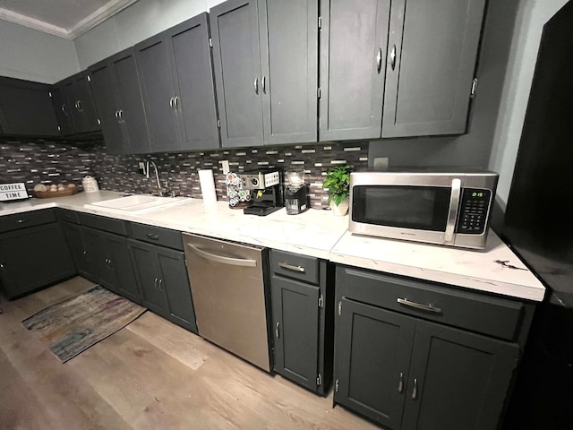 kitchen featuring tasteful backsplash, sink, stainless steel appliances, ornamental molding, and light hardwood / wood-style flooring