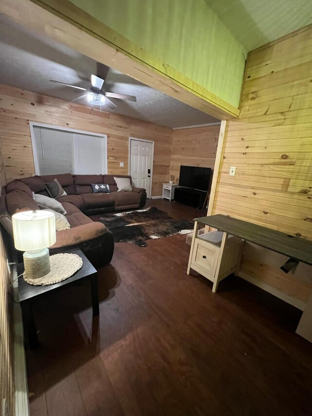 living room featuring dark wood-type flooring, ceiling fan, and wood walls