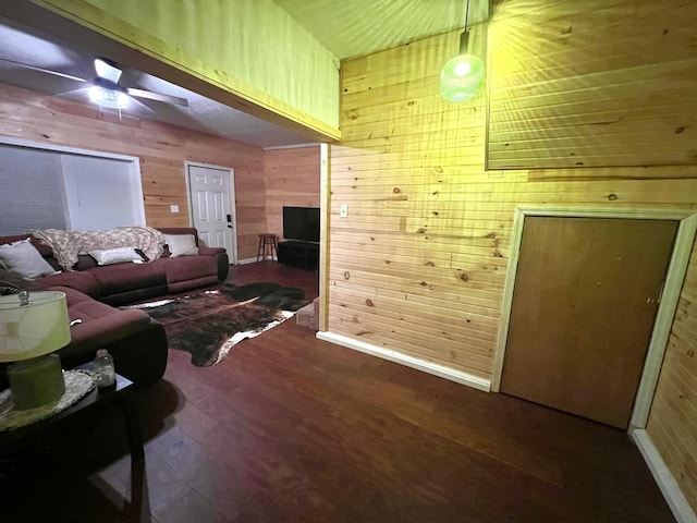 living room with dark wood-type flooring, ceiling fan, and wood walls