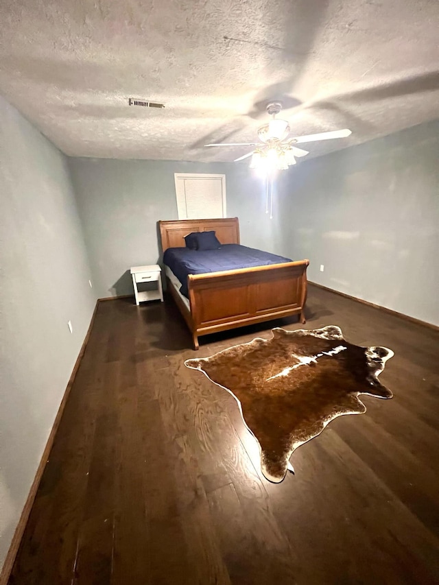 bedroom with a textured ceiling, dark wood-type flooring, and ceiling fan