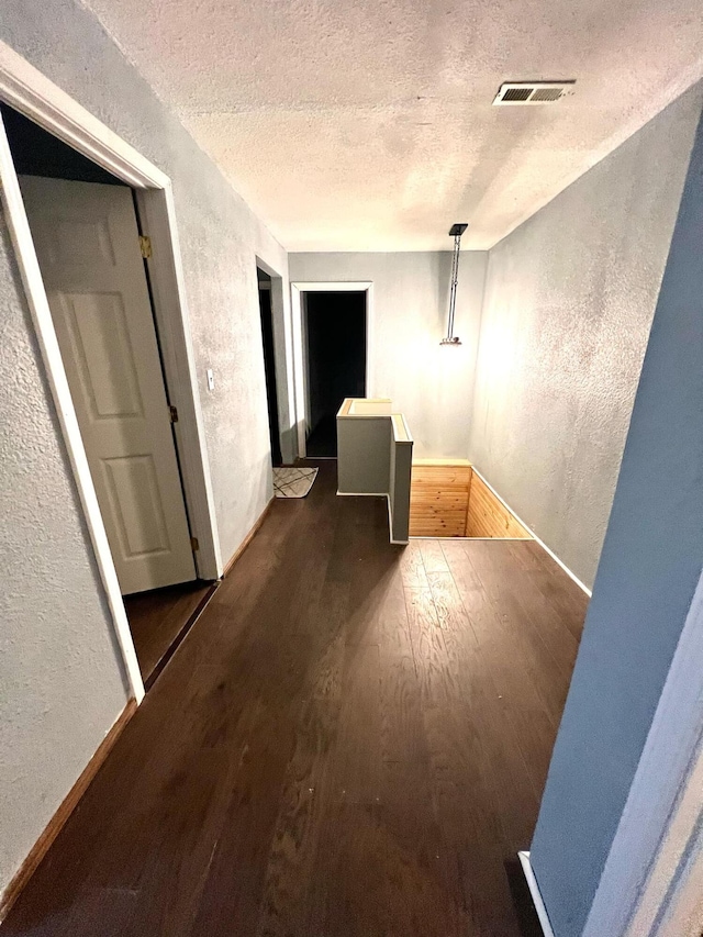 hallway with a textured ceiling and dark hardwood / wood-style flooring