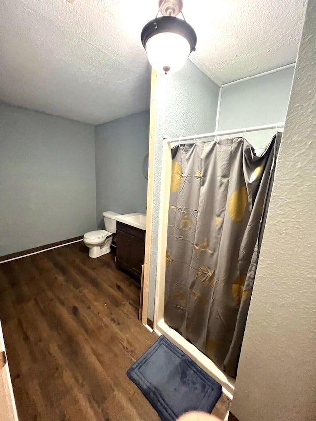 bathroom featuring toilet, wood-type flooring, a shower with shower curtain, vanity, and a textured ceiling