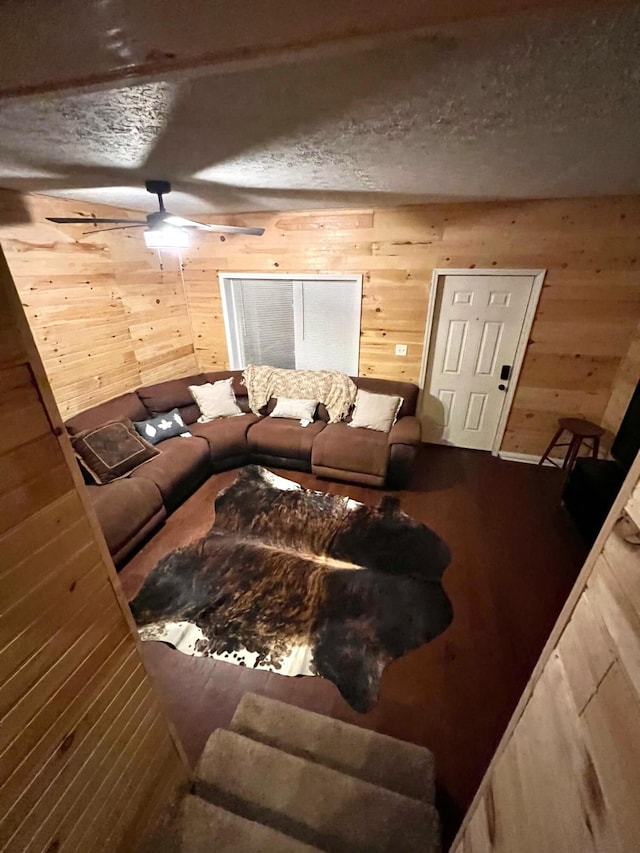 living room featuring a textured ceiling, wooden walls, and ceiling fan