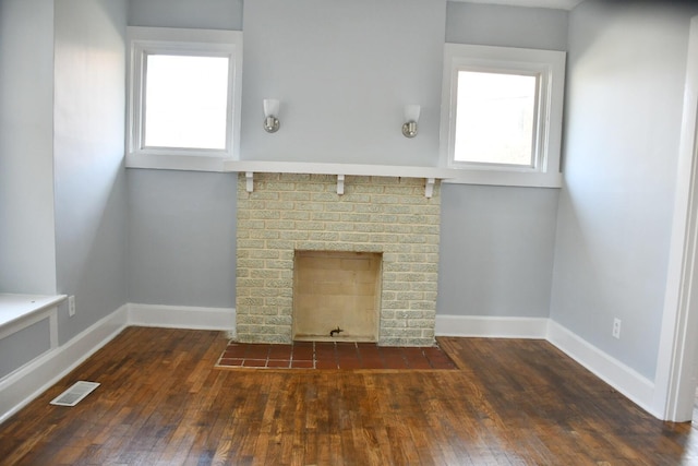 unfurnished living room featuring dark wood-type flooring, a brick fireplace, and plenty of natural light