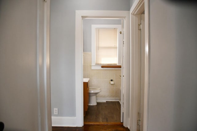 hallway featuring dark wood-type flooring and tile walls