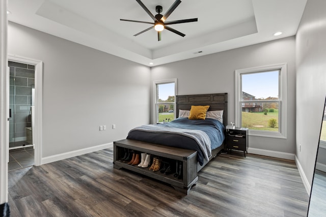 bedroom with ceiling fan, a raised ceiling, dark wood-type flooring, and ensuite bath