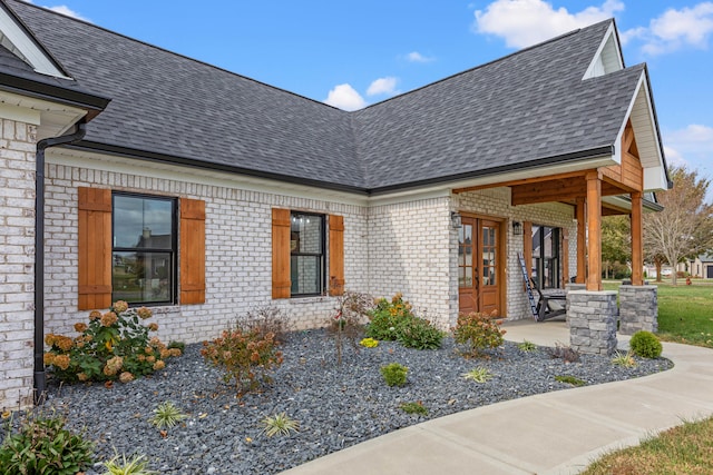 doorway to property featuring a shingled roof and brick siding