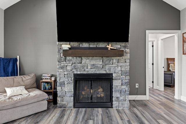 living room with hardwood / wood-style floors, a stone fireplace, and vaulted ceiling